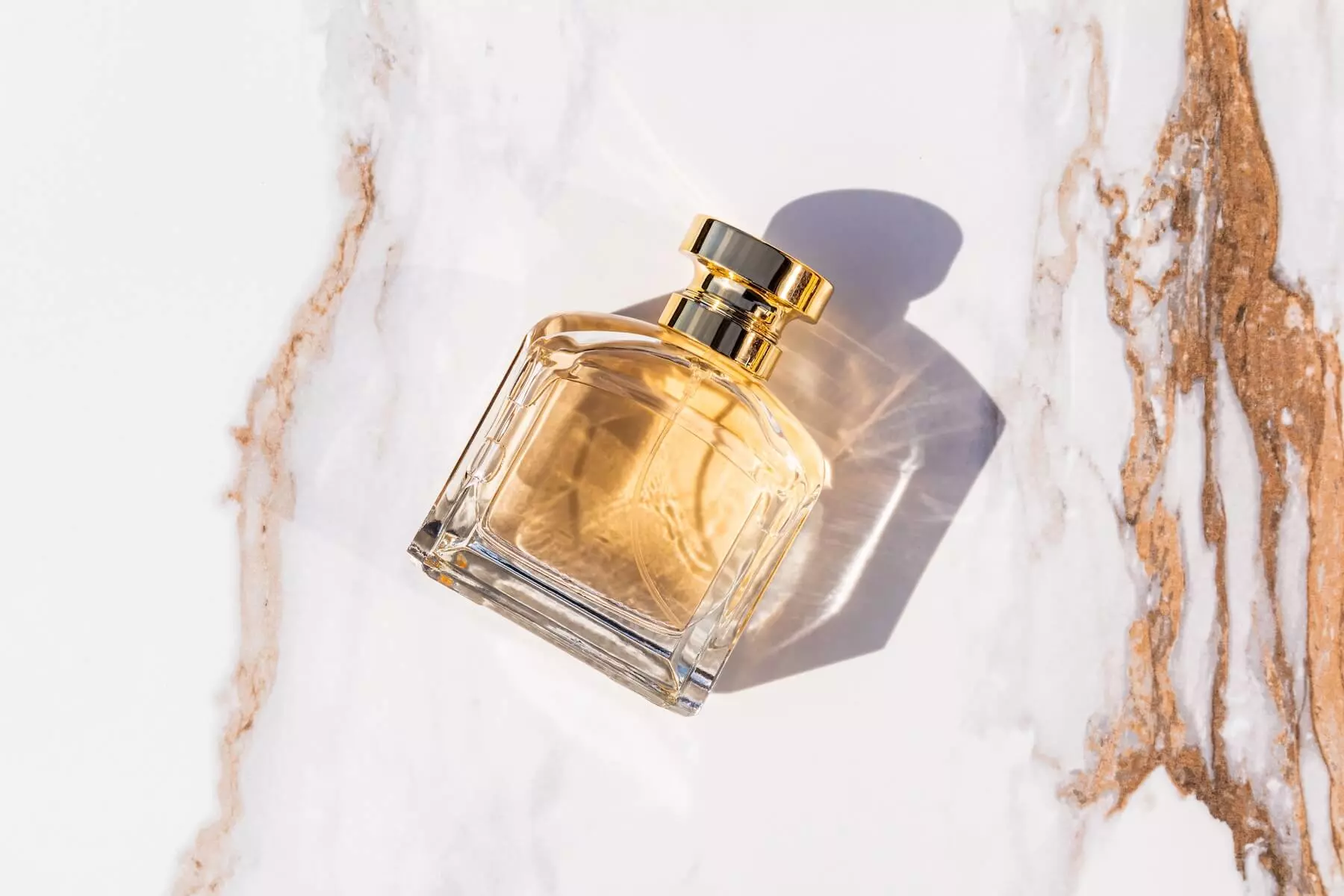 Boccetta di profumo con liquido color oro su fondo bianco marmo