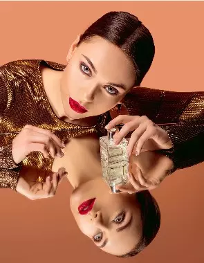 Donna truccata con in mano una boccetta di profumo e la sua immagine nello specchio